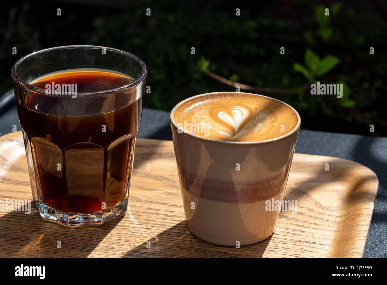 Due tazze di caffè su vassoio di legno con latte art. Tavolo nella caffetteria all'aperto. Concetto di colazione facile. Tazze in ceramica e vetro Foto Stock
