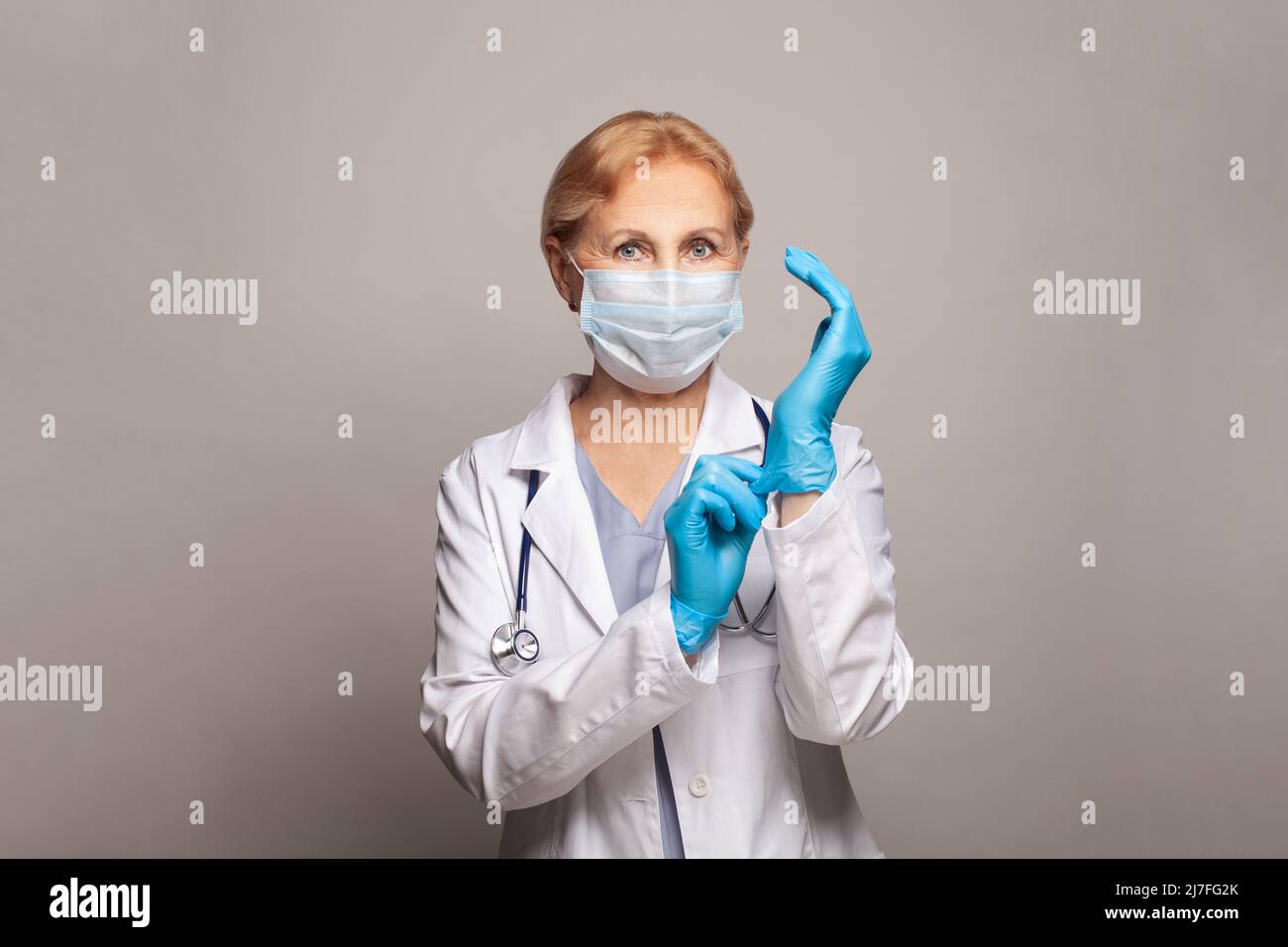 Ritratto di un attraente medico senior in camice bianco e guanti blu Foto Stock