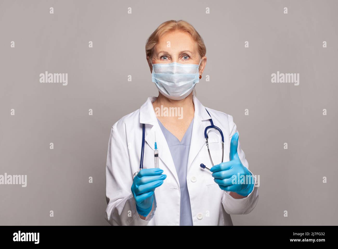 Infermiere femmina maturo o medico che tiene la siringa e mostra il pollice in su Foto Stock