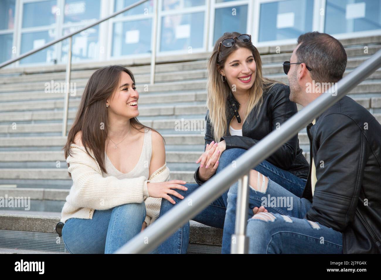 gruppo di tre giovani amici che parlano seduti su delle scale e che hanno un buon tempo. concetto di amicizia persone reali Foto Stock