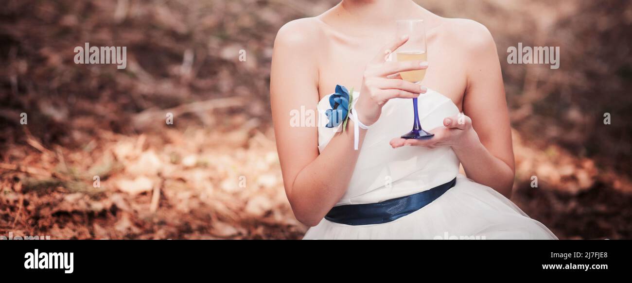 bella sposa con un bicchiere di vino seduto nel parco primaverile Foto Stock