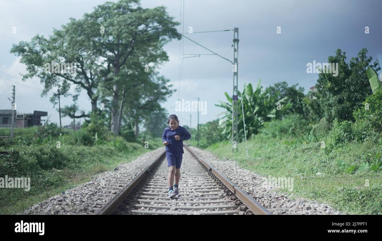 Indian Kid che corre sulla pista ferroviaria nella gamma Himalayan dell'India, verde sullo sfondo. Allenamento fisico. Foto di alta qualità Foto Stock