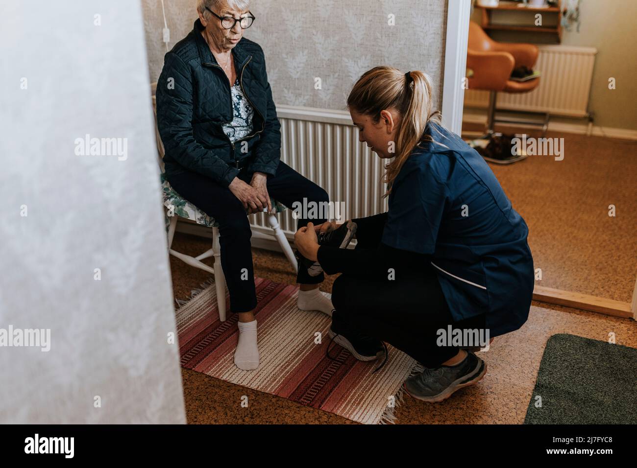 Domestico caretaker che aiuta la donna anziana ha messo sulle scarpe Foto Stock