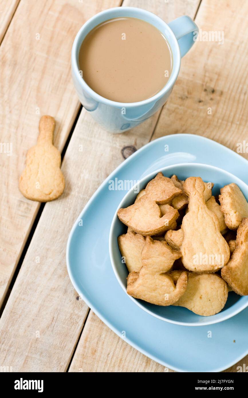 Dolci e gustosi biscotti nel piatto blu, una tazza di caffè con latte e taccuino su sfondo in legno non dipinto. Foto Stock