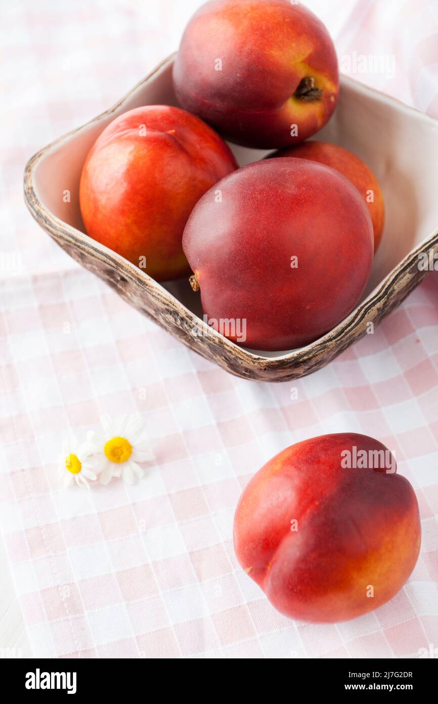 Le nettarine succose e mature si trovano in un piatto fatto a mano su una tovaglia in una cella Foto Stock