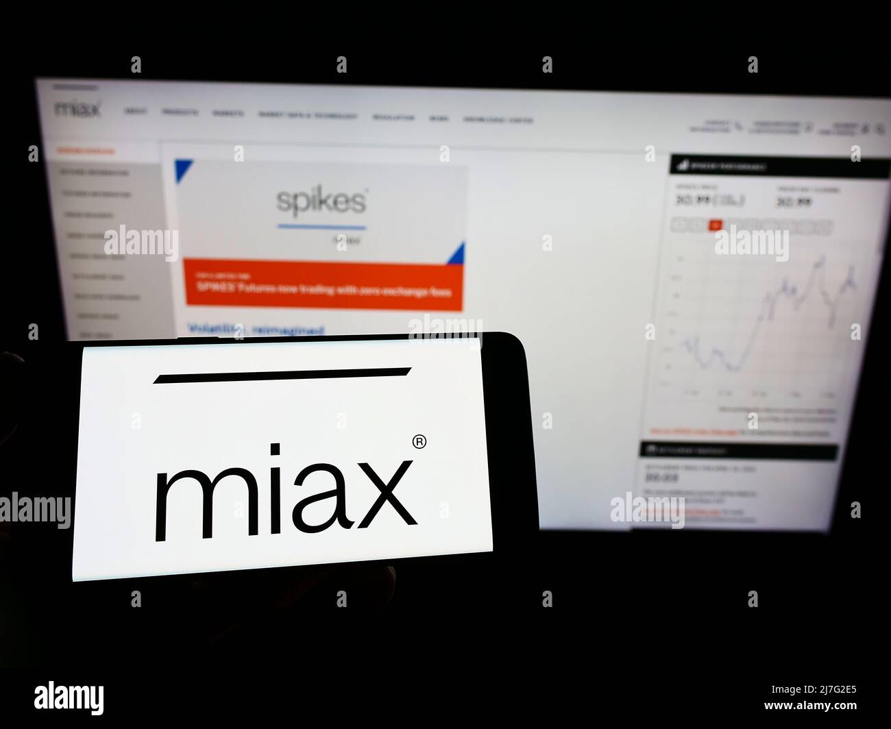Persona che tiene uno smartphone con il logo di Miami International Securities Exchange (MIAX) sullo schermo di fronte al sito Web. Mettere a fuoco sul display del telefono. Foto Stock