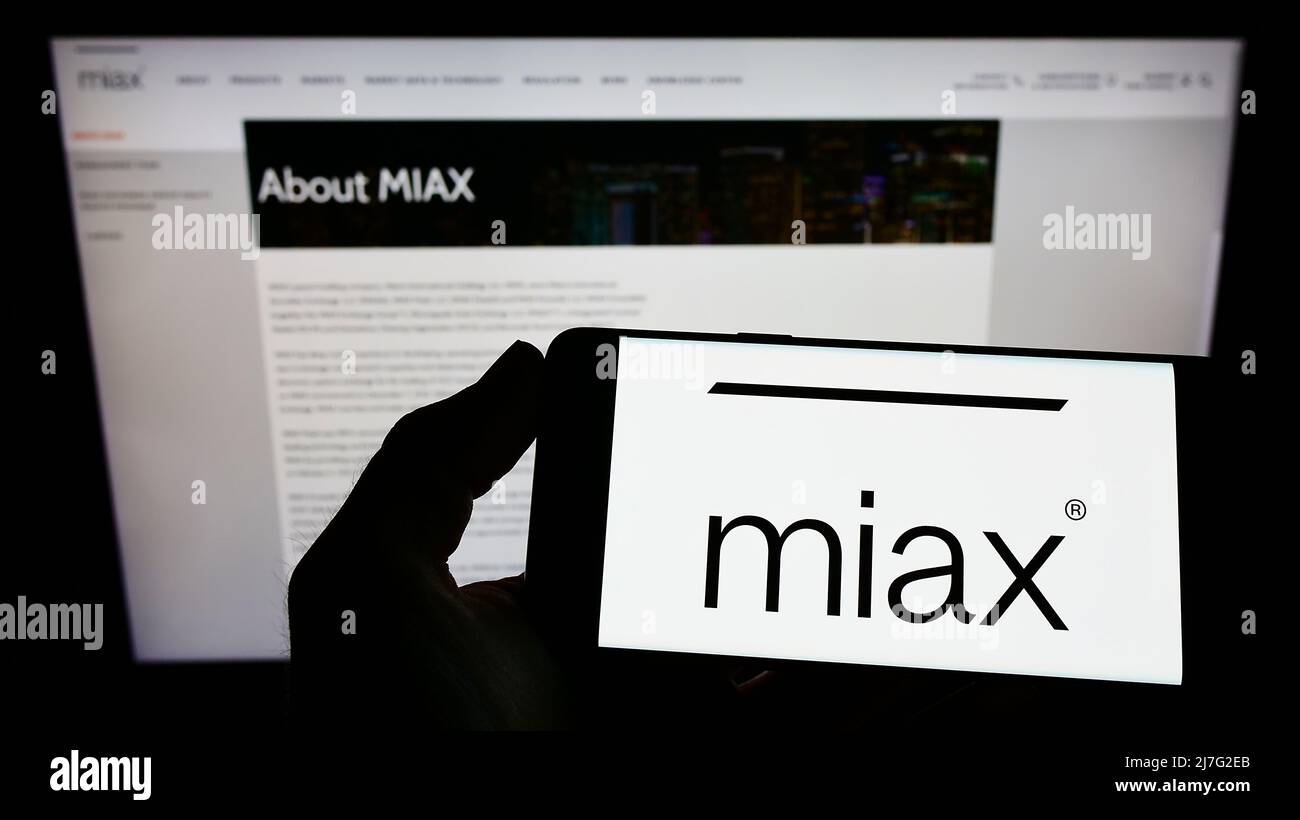 Persona che detiene il telefono cellulare con il logo di Miami International Securities Exchange (MIAX) sullo schermo di fronte alla pagina web. Mettere a fuoco sul display del telefono. Foto Stock