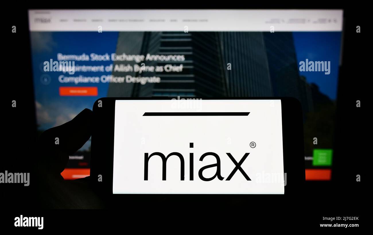 Persona che tiene il cellulare con il logo di Miami International Securities Exchange (MIAX) sullo schermo di fronte alla pagina web. Mettere a fuoco sul display del telefono. Foto Stock