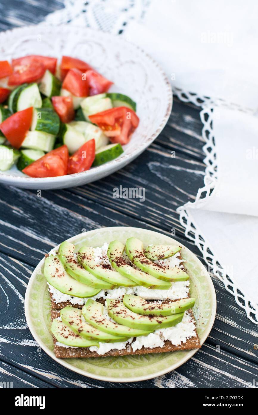 Una sana insalata di pomodori e verdure fresche e un sandwich fatto in casa con formaggio morbido, avocado e condimento sul pane tostato di grano duro. Una colazione sana Foto Stock