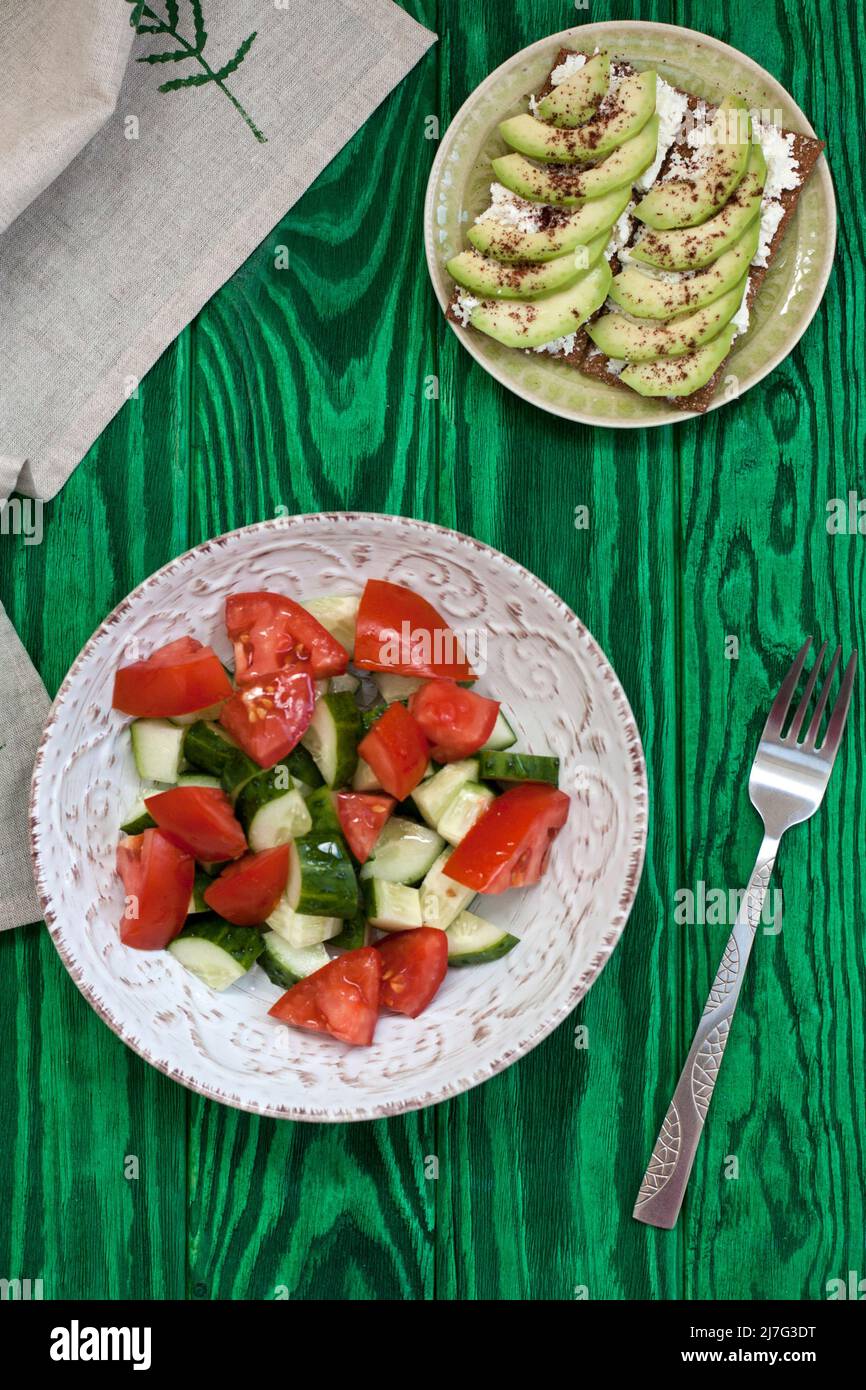 Una sana insalata di pomodori e verdure fresche e un sandwich fatto in casa con formaggio morbido, avocado e condimento sul pane tostato di grano duro. Una colazione sana Foto Stock