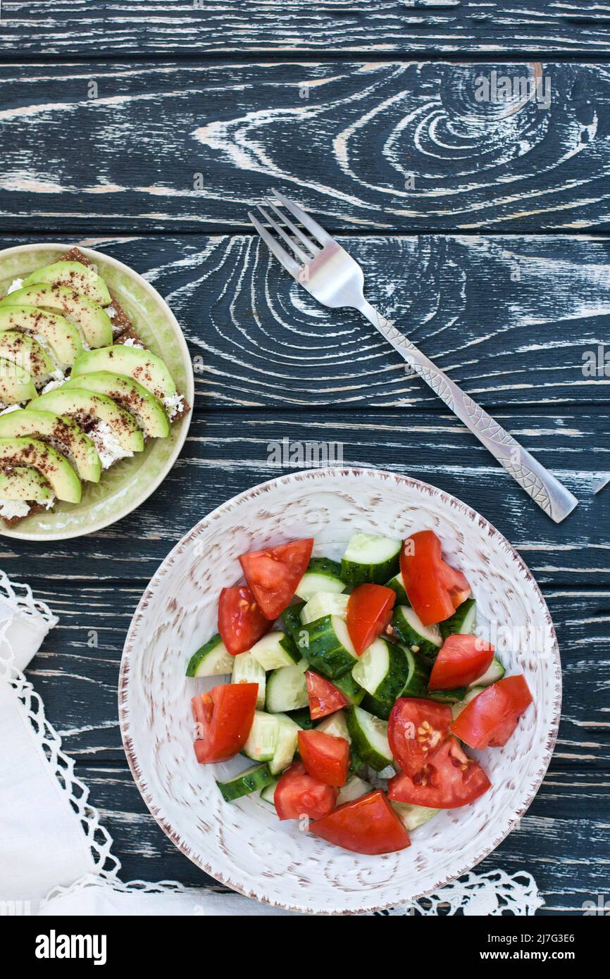 Una sana insalata di pomodori e verdure fresche e un sandwich fatto in casa con formaggio morbido, avocado e condimento sul pane tostato di grano duro. Una colazione sana Foto Stock