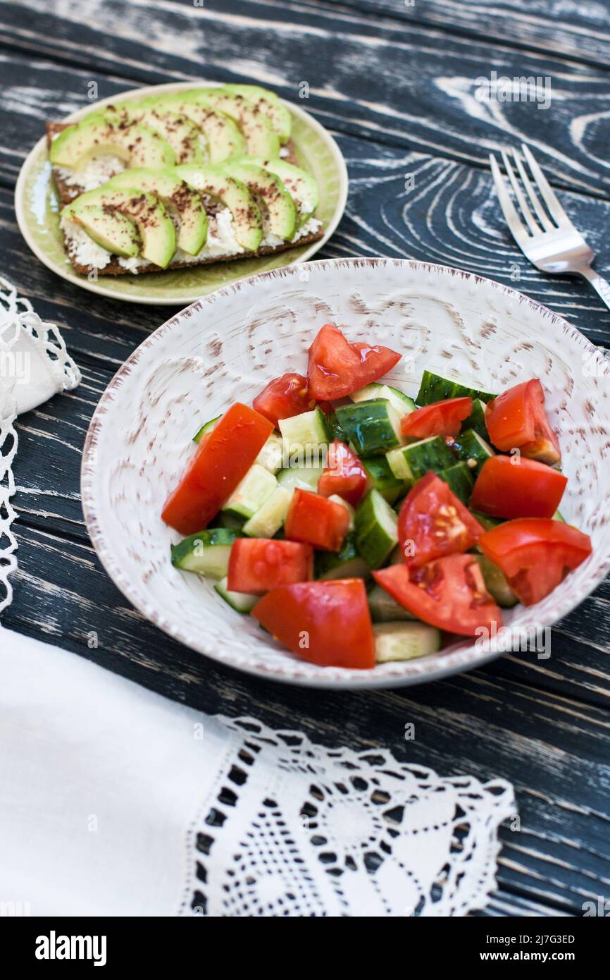 Una sana insalata di pomodori e verdure fresche e un sandwich fatto in casa con formaggio morbido, avocado e condimento sul pane tostato di grano duro. Una colazione sana Foto Stock