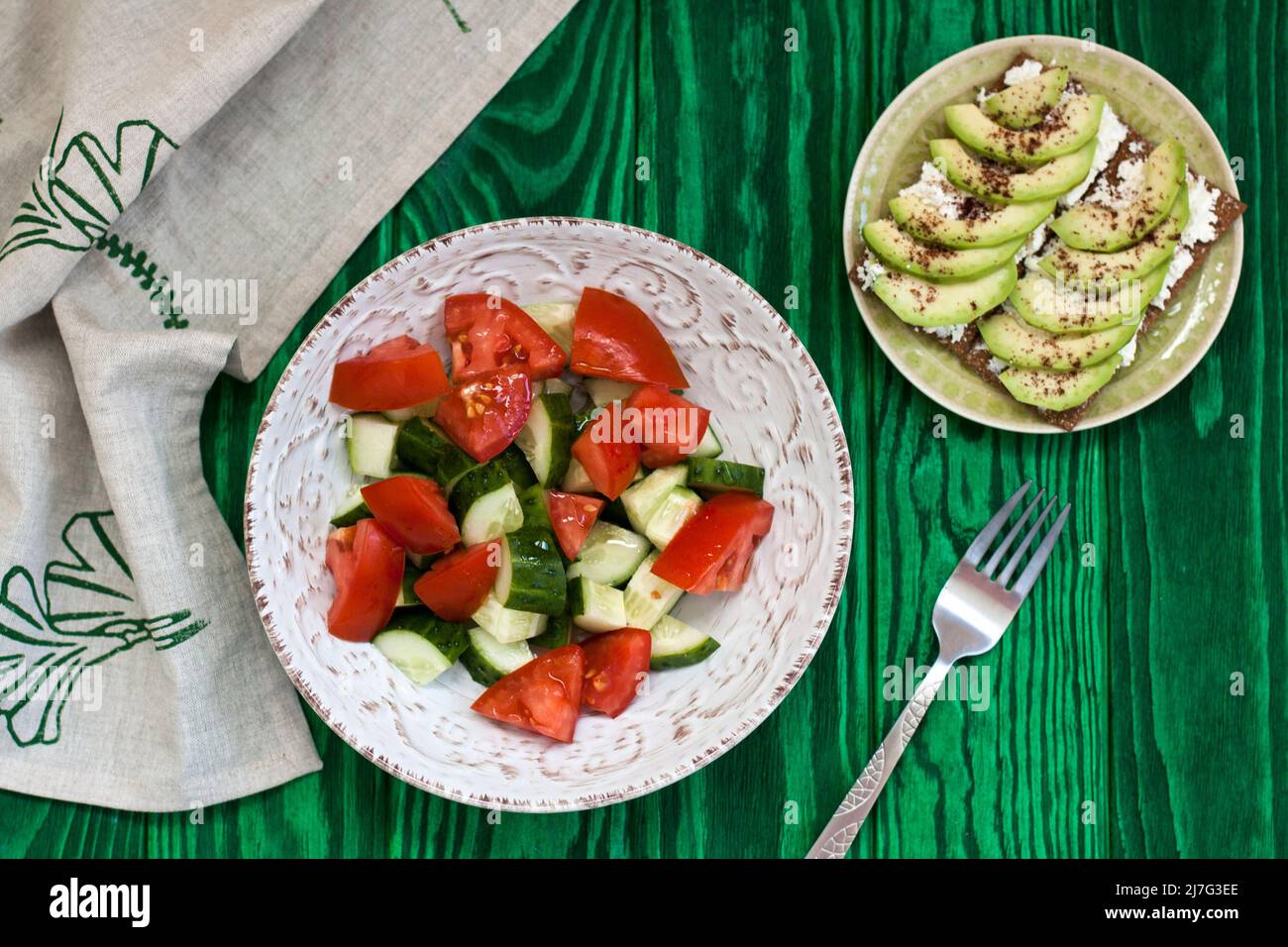 Una sana insalata di pomodori e verdure fresche e un sandwich fatto in casa con formaggio morbido, avocado e condimento sul pane tostato di grano duro. Una colazione sana Foto Stock