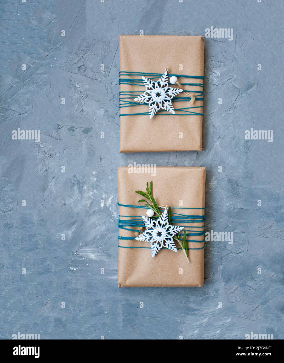 Due regali di Natale in carta artigianale avvolta in filo blu con fiocchi  di neve bianchi e ramificazioni di rosmarino su sfondo grigio di cemento. C'è  un posto Foto stock - Alamy