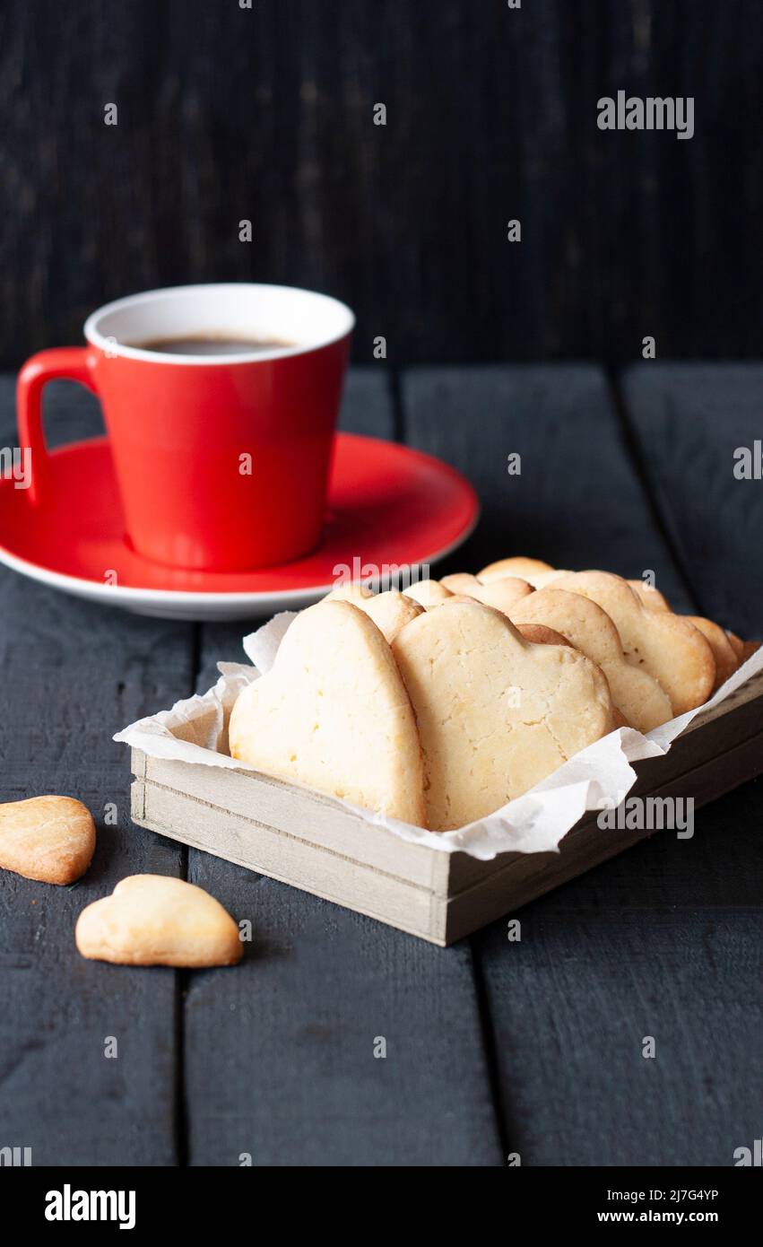 Bicchiere rosso e cuori di biscotti su sfondo nero Foto Stock