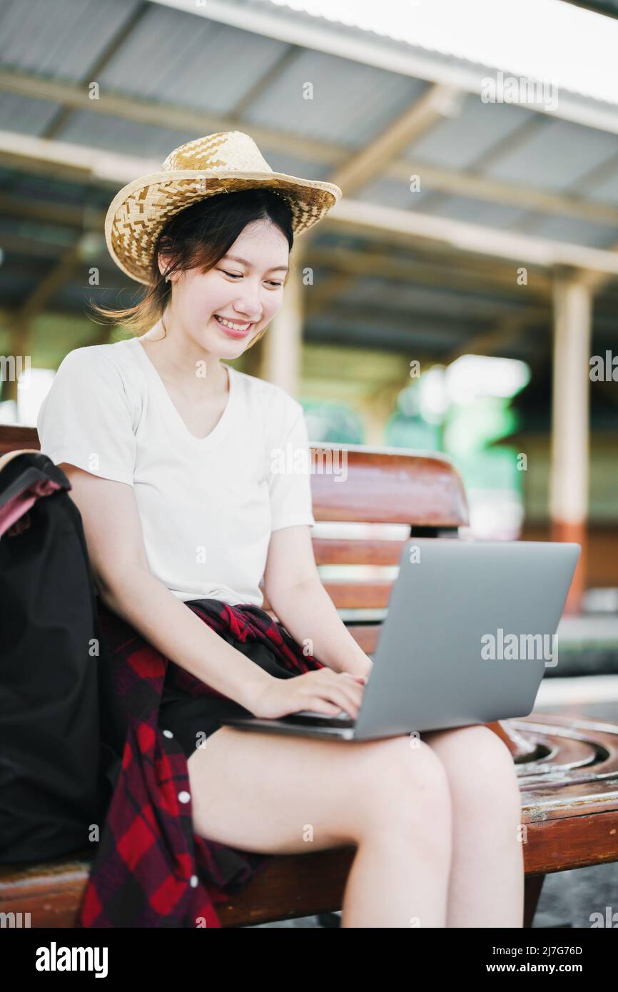 Estate, relax, vacanza, viaggio, ritratto di bella ragazza asiatica utilizzando il computer portatile alla stazione ferroviaria, in attesa del loro tempo di viaggio. Foto Stock