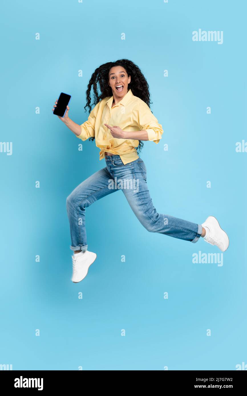 Signora allegra che salta e punta allo schermo vuoto dello smartphone Foto Stock