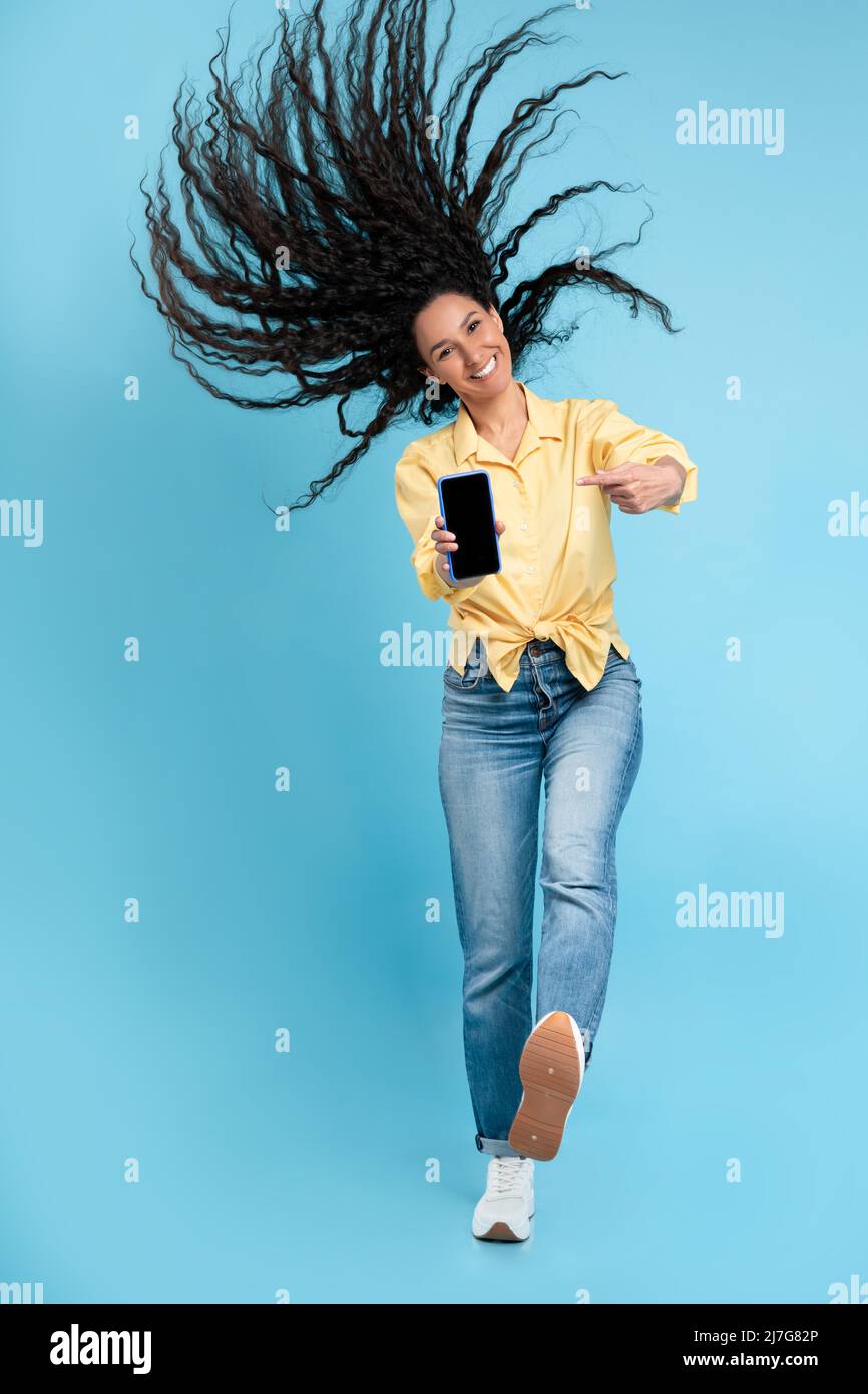 Signora allegra che salta e punta allo schermo vuoto dello smartphone Foto Stock