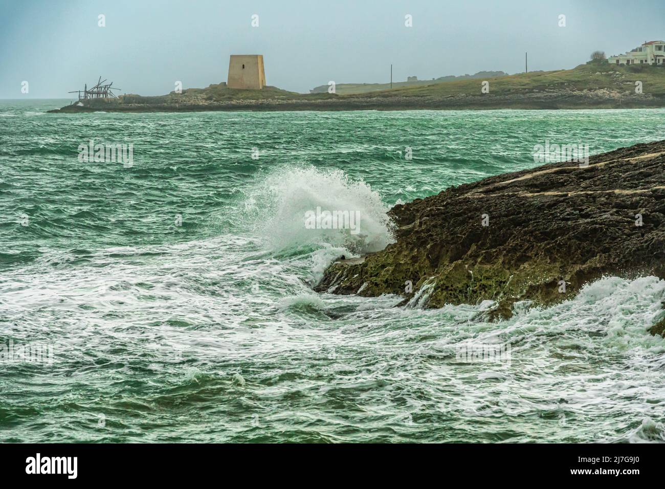 Il mare tempestoso si schianta contro le coste rocciose della Puglia, sullo sfondo la torre di Gusmay, una torre di guardia e un trabucco. Peschici, Puglia Foto Stock