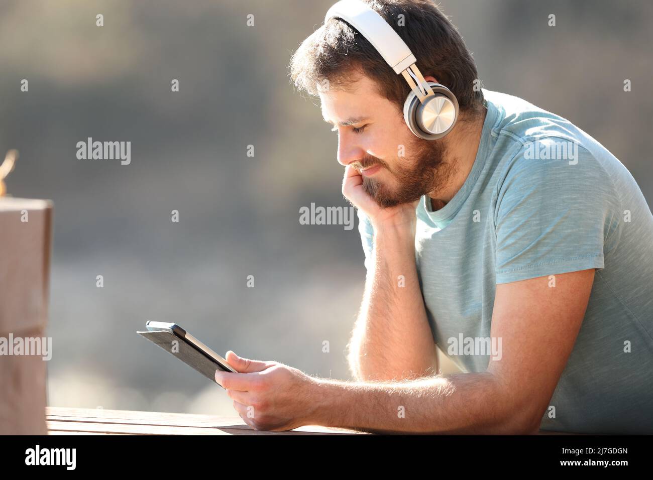 Profilo di un uomo soddisfatto che guarda i video sul tablet con le cuffie in natura Foto Stock