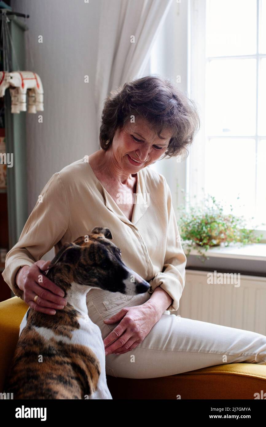 Donna anziana che accarezzava il cane mentre si siede a casa Foto Stock