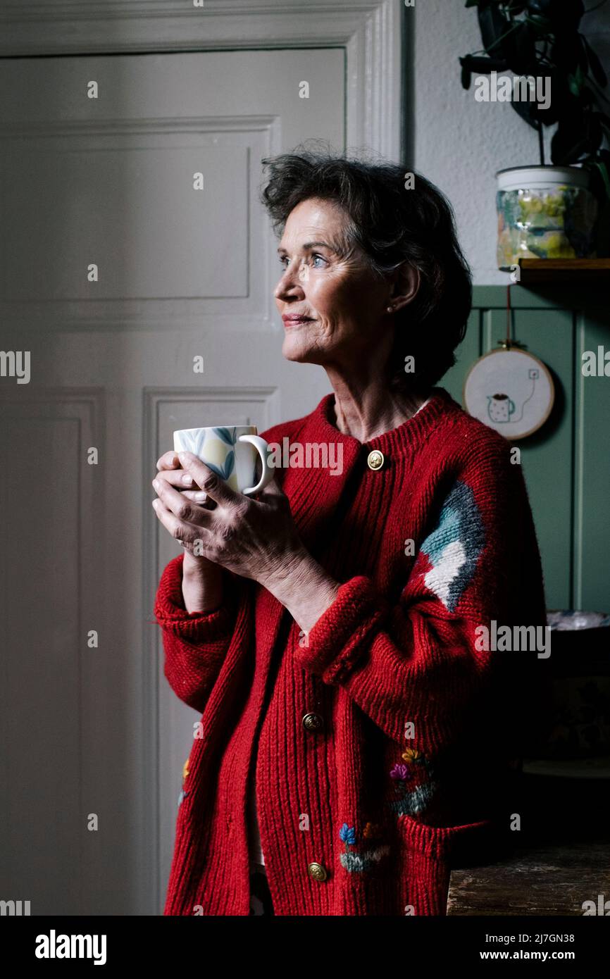 Sorridente anziana che contempla mentre si alza in cucina a casa Foto Stock