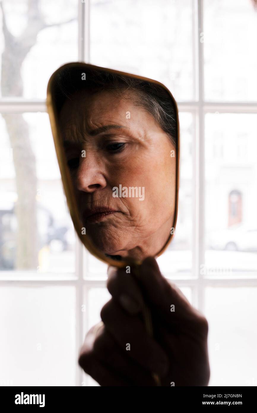 Faccia rugosa della donna anziana sullo specchio della mano Foto Stock