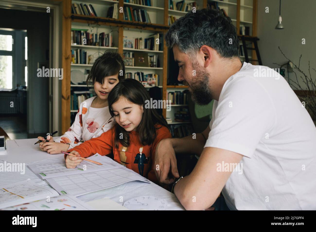 Le ragazze gemelle che fanno i compiti mentre si siedono dal padre al tavolo Foto Stock