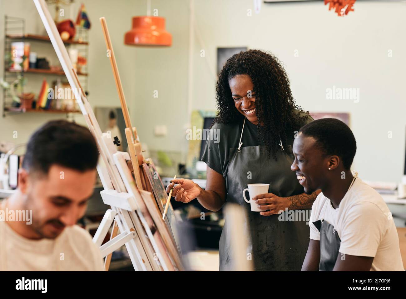 Allegra tutor femminile con giovane studente davanti alla pittura in classe d'arte Foto Stock