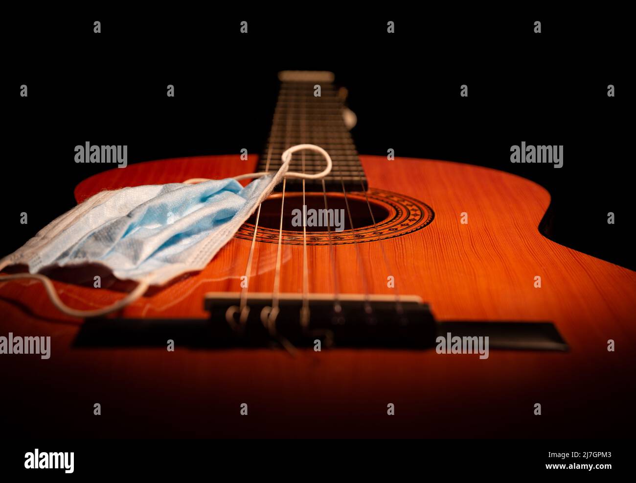 Corpo di chitarra acustica spagnolo in primo piano con una maschera pandemica covid su sfondo nero Foto Stock