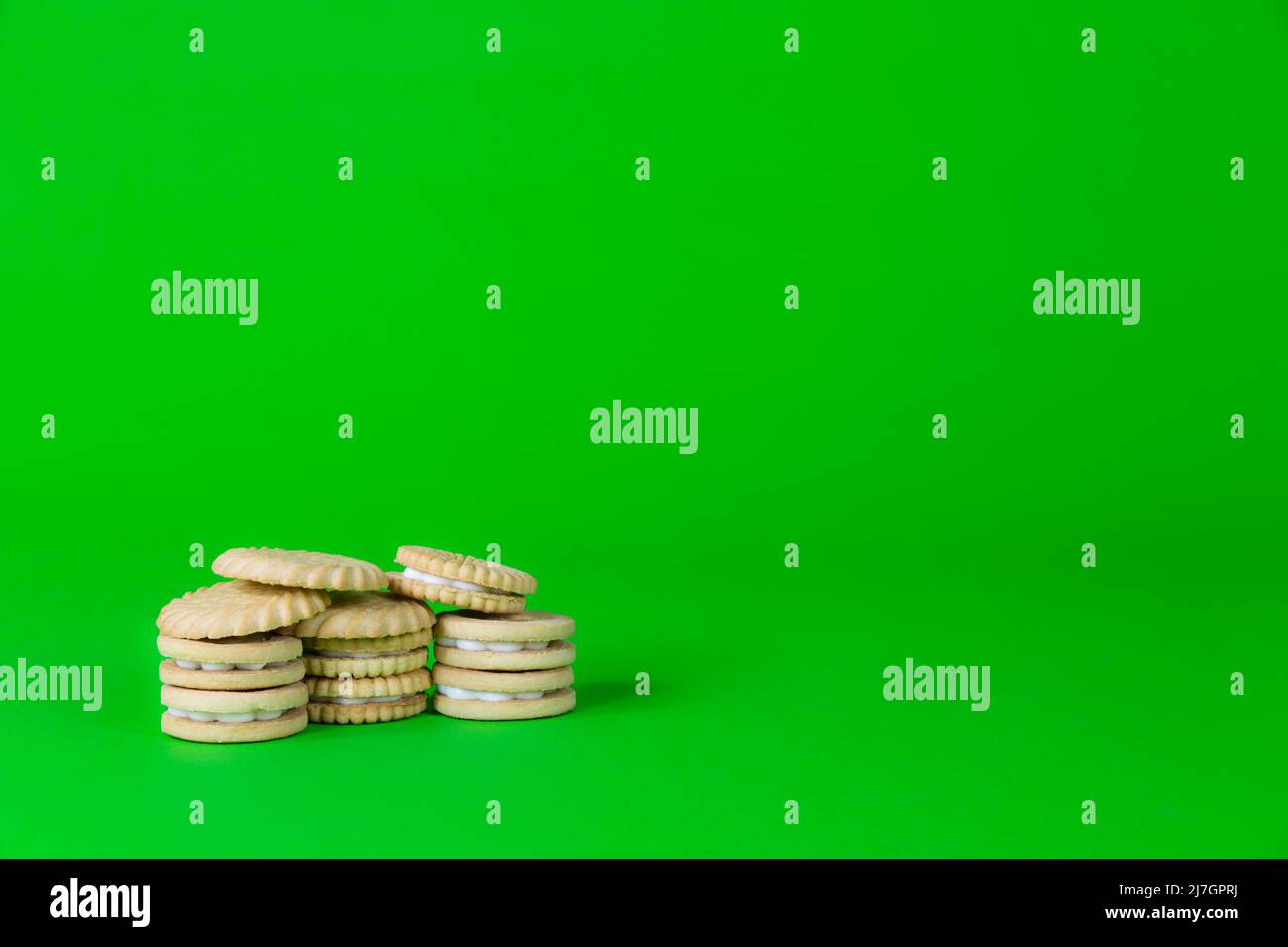 Pile di biscotti biscotti su sfondo verde brillante per stile di vita malsano aumento di peso e concetti di perdita. Foto Stock