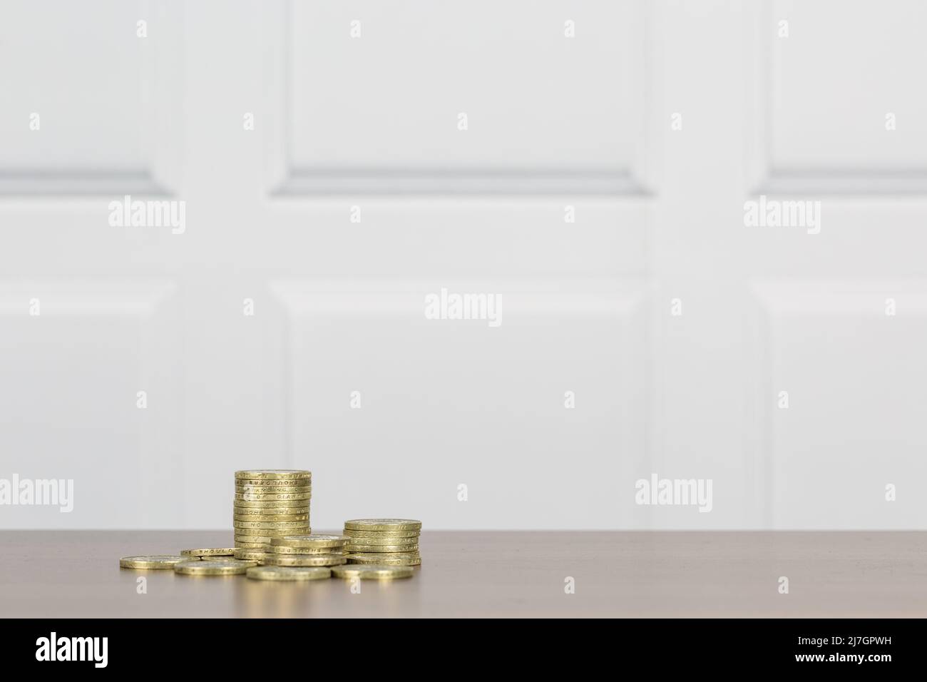 UK British Pound Sterling GBP pile di monete color oro e caduti in contanti, su una superficie di legno con parete a pannelli bianchi per una copia pulita Foto Stock