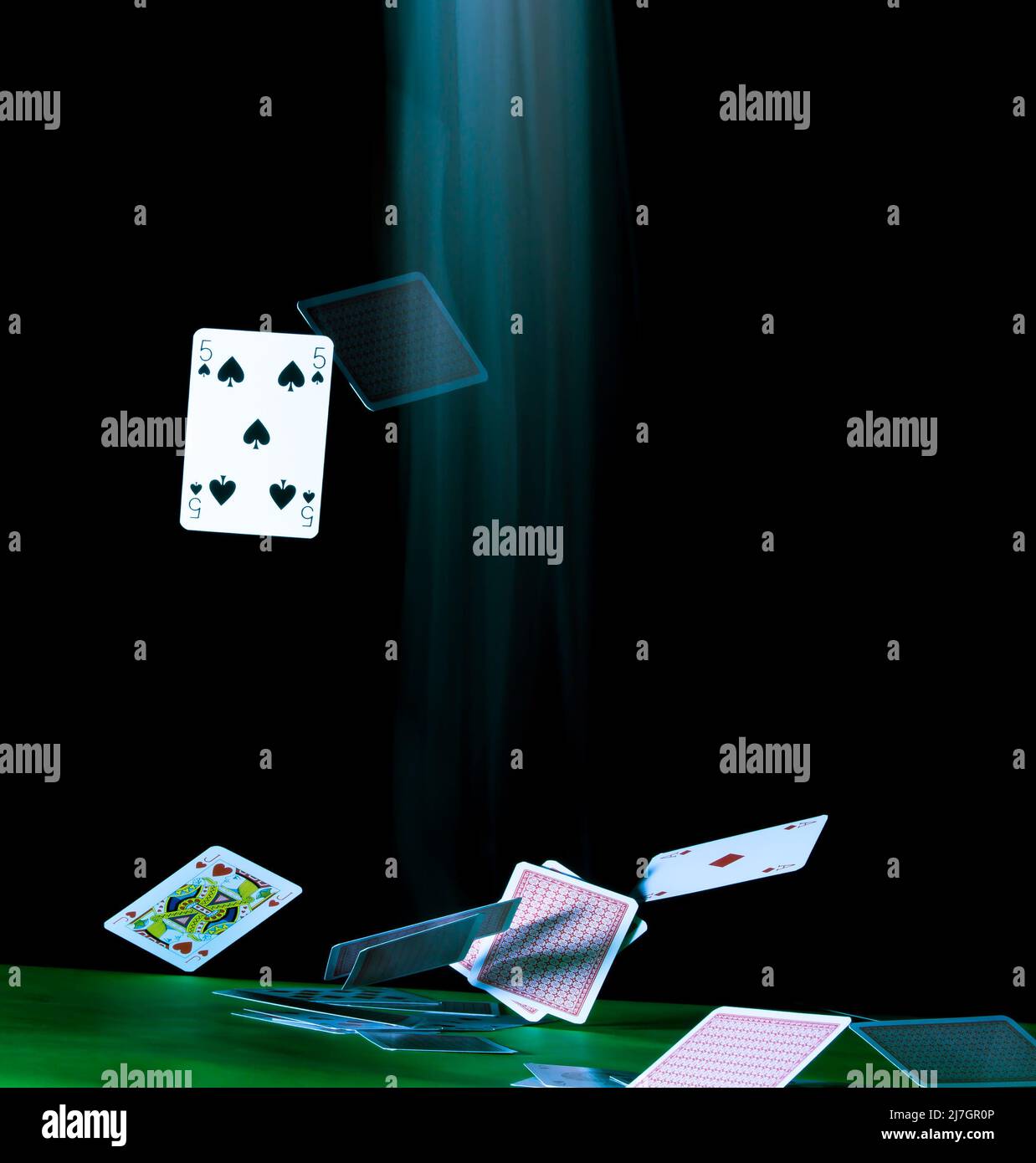 Carte da gioco che cadono al rallentatore su un tavolo con tracce di movimento sfocate, con spazio per la copia di un poster, su sfondo nero. Foto Stock