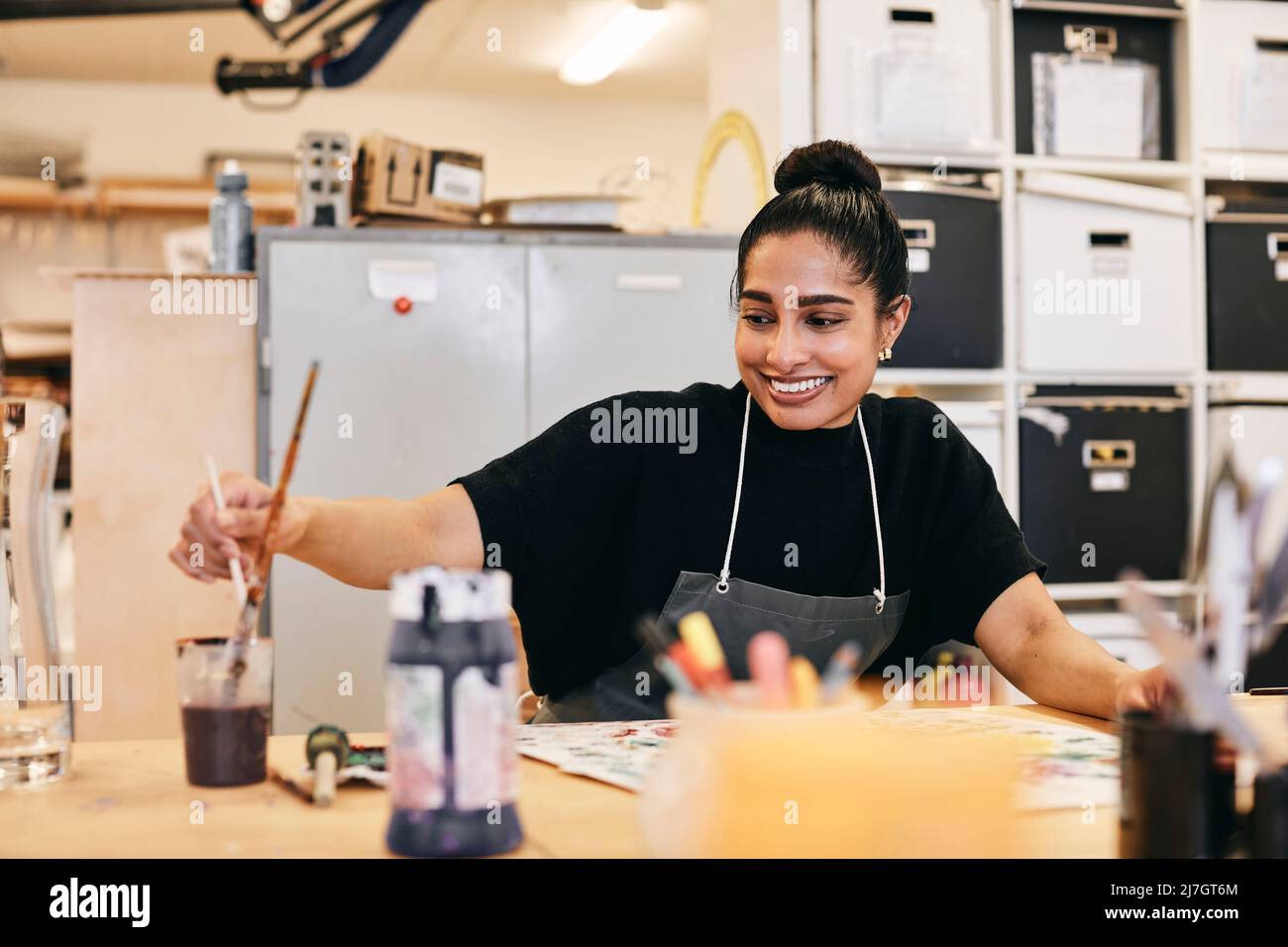Studentessa sorridente in pittura grembiale a tavola in classe d'arte Foto Stock