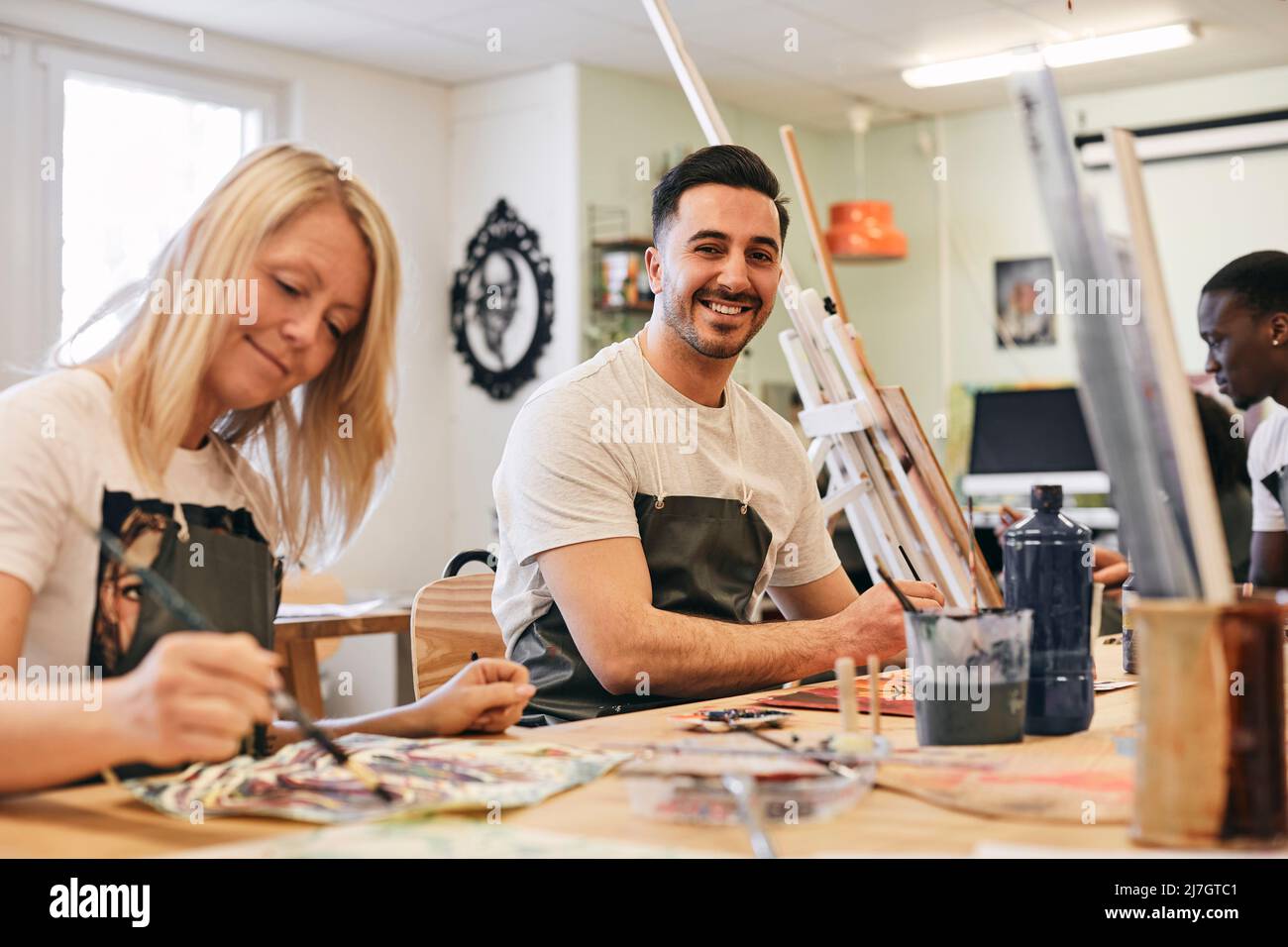 Ritratto di giovane felice seduto da femmina studente pittura a tavola in classe d'arte Foto Stock