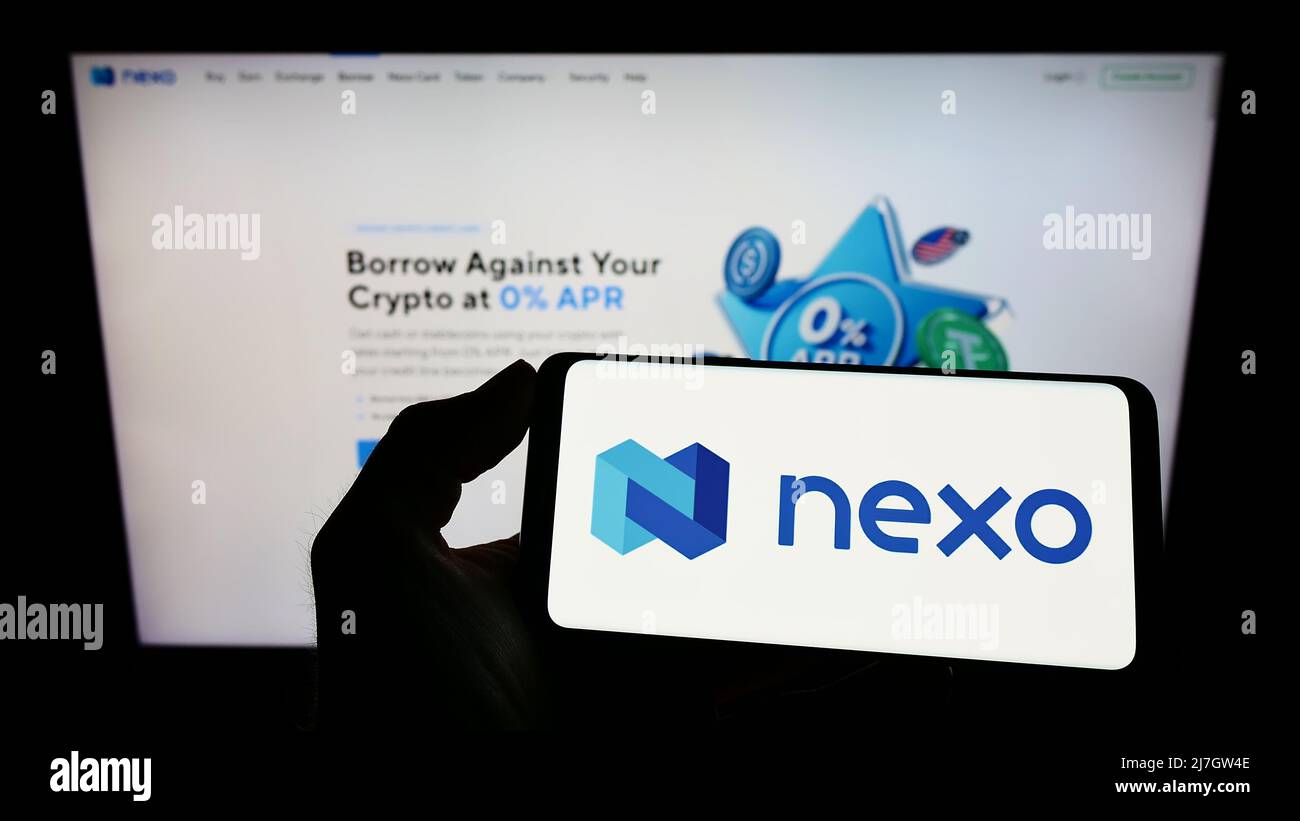 Persona che tiene il cellulare con il logo della società britannica di asset digitali Nexo (nexo.io) sullo schermo di fronte alla pagina web. Mettere a fuoco sul display del telefono. Foto Stock
