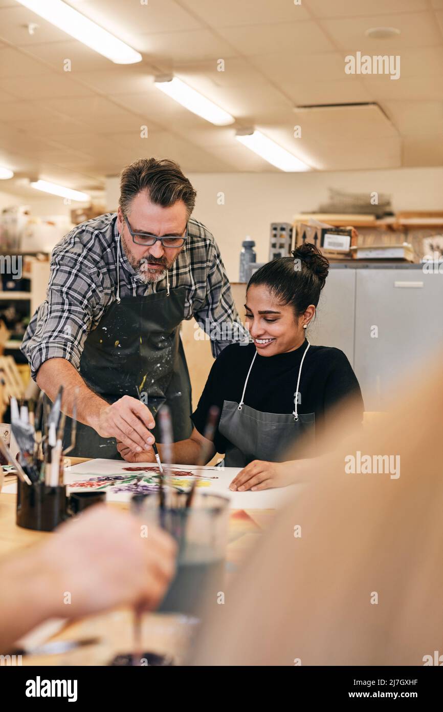 Istruttore con pennello che insegna lo studente seduto al tavolo in classe d'arte Foto Stock