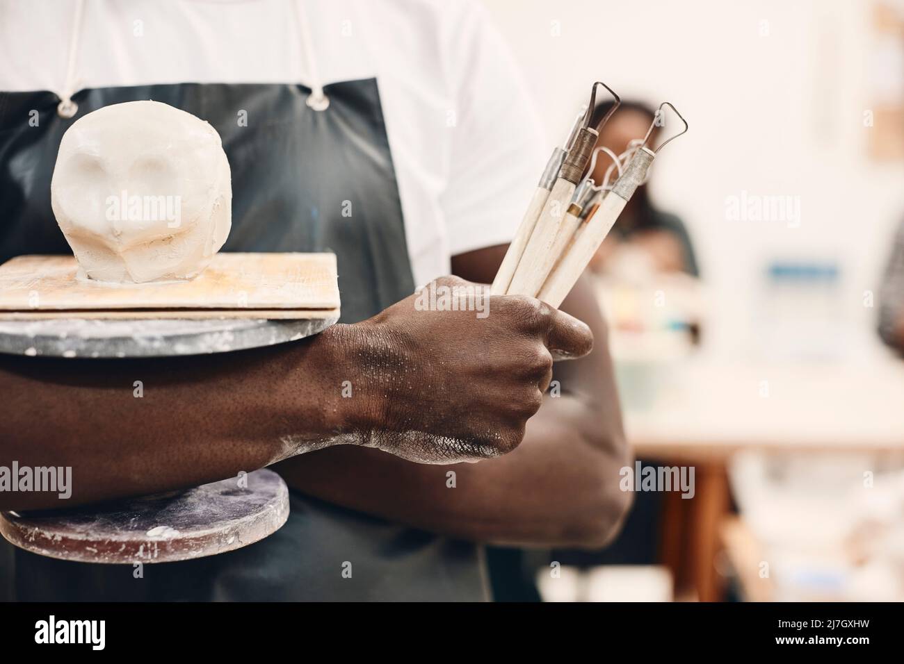 Sezione centrale del giovane uomo che tiene gli attrezzi di lavoro e l'argilla modellata nella classe dell'arte Foto Stock