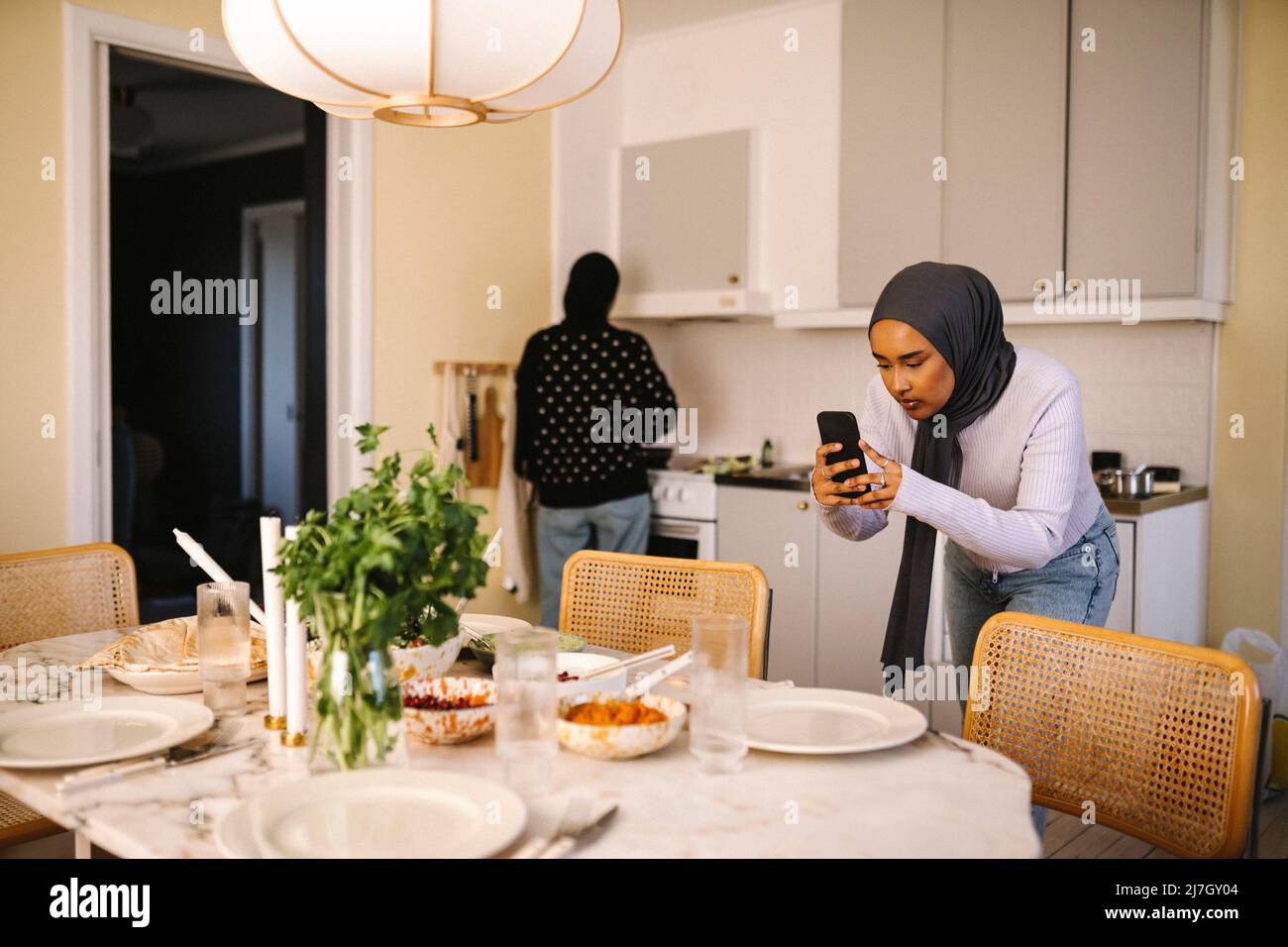 Giovane donna che fotografa il cibo attraverso il telefono cellulare mentre un amico cucinava in cucina a casa Foto Stock