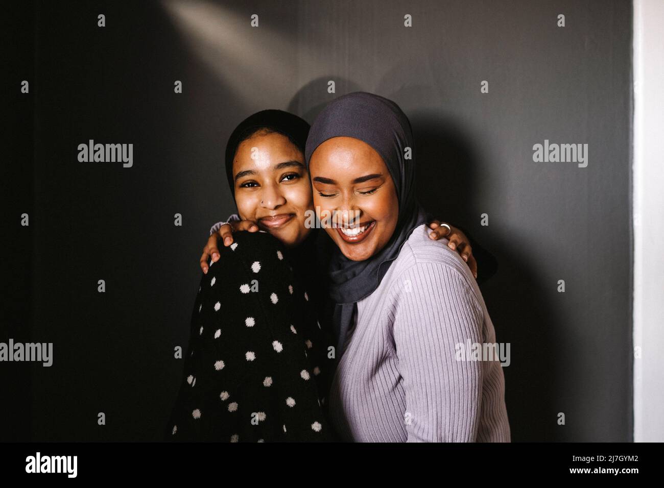 Giovane donna sorridente che abbraccia un amico con gli occhi chiusi su sfondo grigio Foto Stock