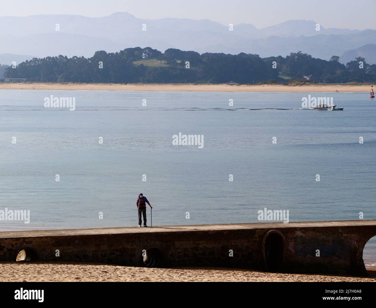 Paesaggio vista di un uomo con un bastone a piedi su un molo di pietra nella baia di Santander Cantabria Spagna Primavera mattina presto Foto Stock