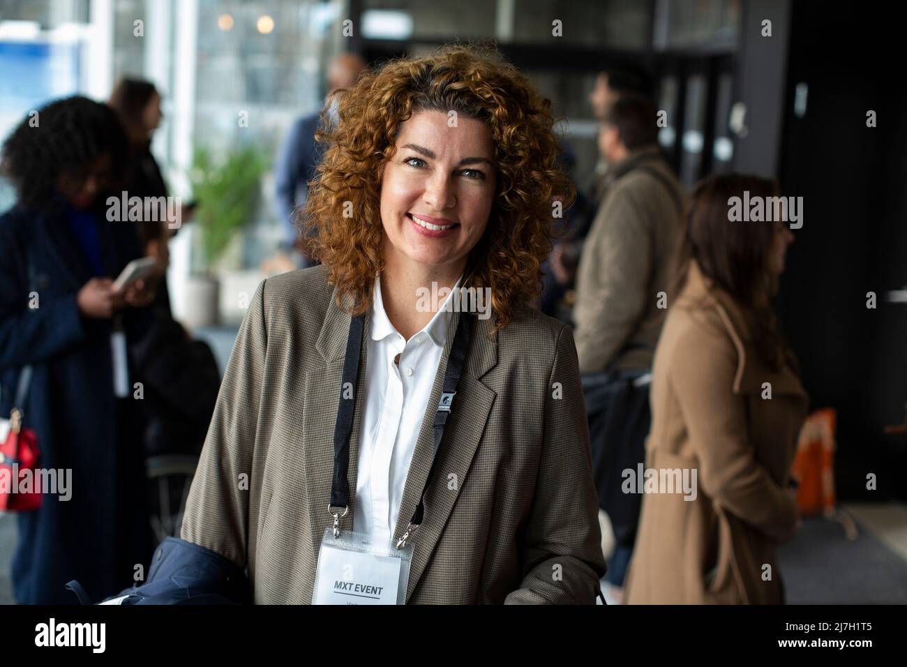 Donna d'affari sorridente con capelli marroni ricci al centro congressi durante il seminario Foto Stock