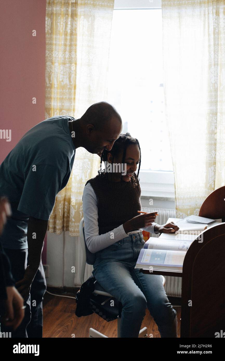 Vista laterale del padre che assiste la figlia in compiti a casa Foto Stock