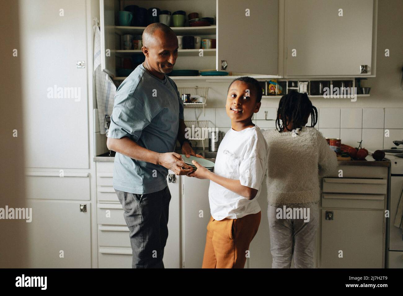 Figlio che aiuta il padre mentre tiene i piatti in cucina a casa Foto Stock