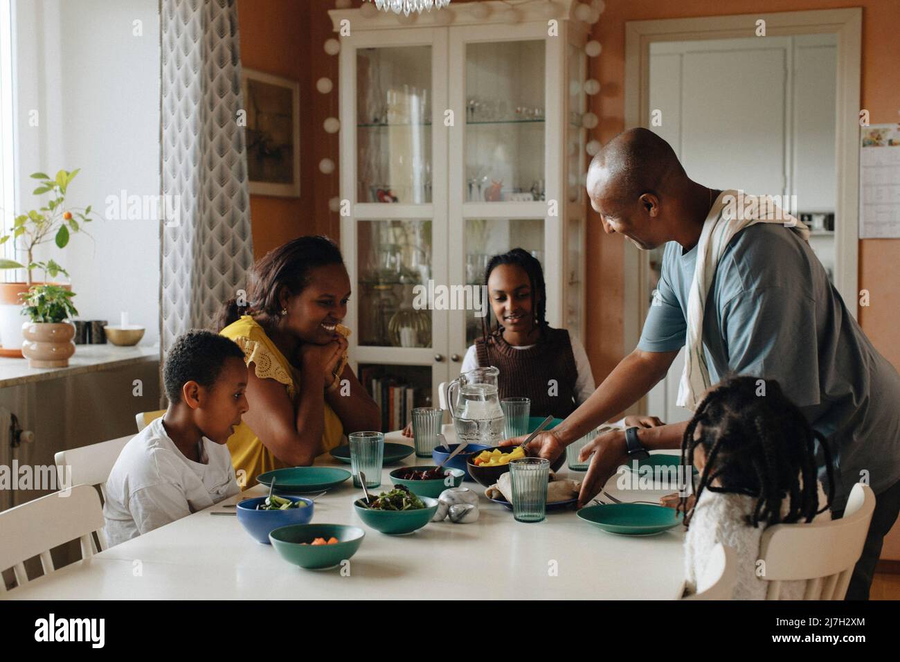 Una famiglia felice che guarda il cibo servito dall'uomo al tavolo da pranzo Foto Stock