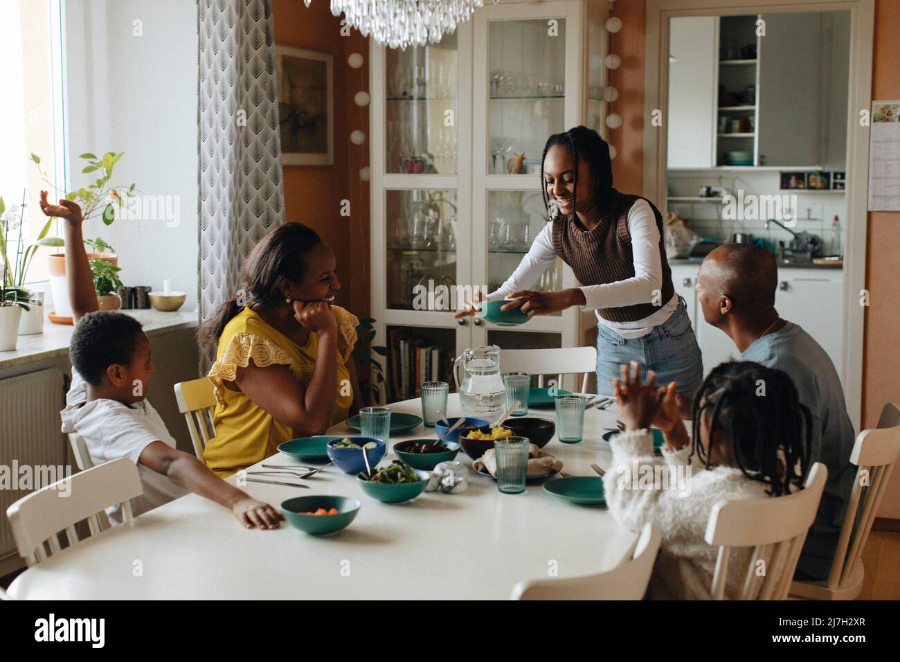 Ragazza che serve cibo per la famiglia seduto al tavolo da pranzo Foto Stock