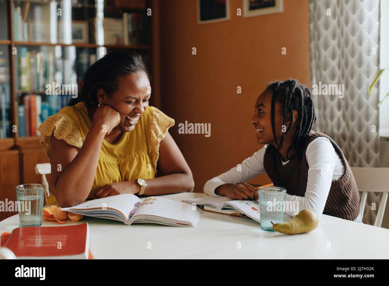 Figlia felice guardando la madre ridendo mentre si siede al tavolo Foto Stock