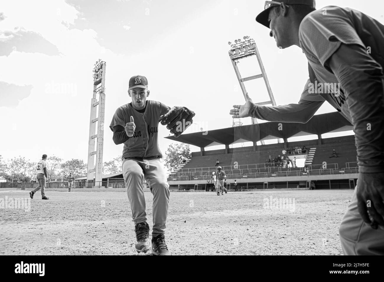 Il giocatore cubano di baseball corre verso il dugout dando il segno dei pollici e il suo allenatore si allunga per scuotere la mano. Foto Stock