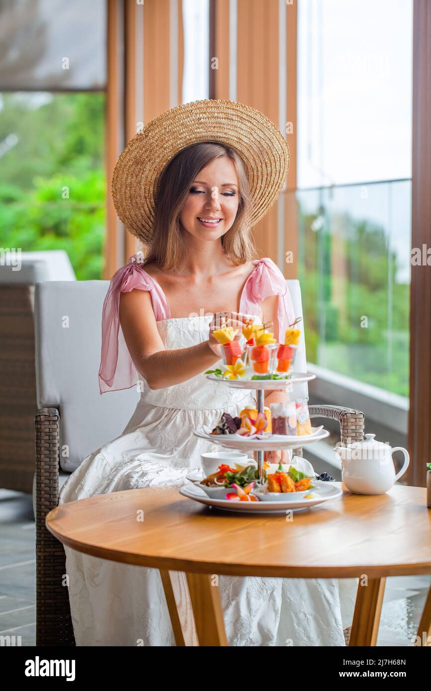 Tè pomeridiano in un ristorante di lusso con vista mare. Donna elegante che mangia frutta Foto Stock