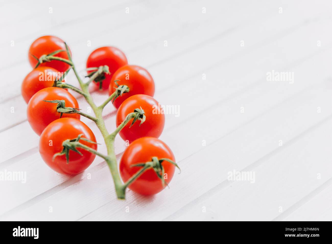 Pomodori ciliegini maturi succosi su un rametto verde su uno sfondo bianco di legno. Cibo vegetariano sano e sano. CopySpace. Foto Stock